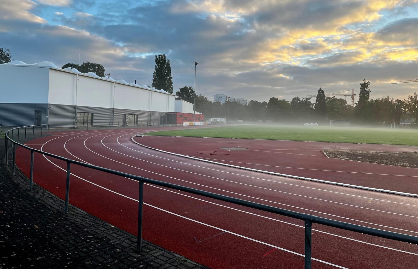 Sportplatz mit Laufbahn, verschwommener Rasenfläche und einem modernen Gebäude im Hintergrund bei nebligem Wetter.