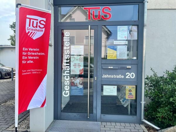 Eingang zur Geschäftsstelle des TuS Griesheim mit einer roten Fahne und Informationen an der Glasfront.