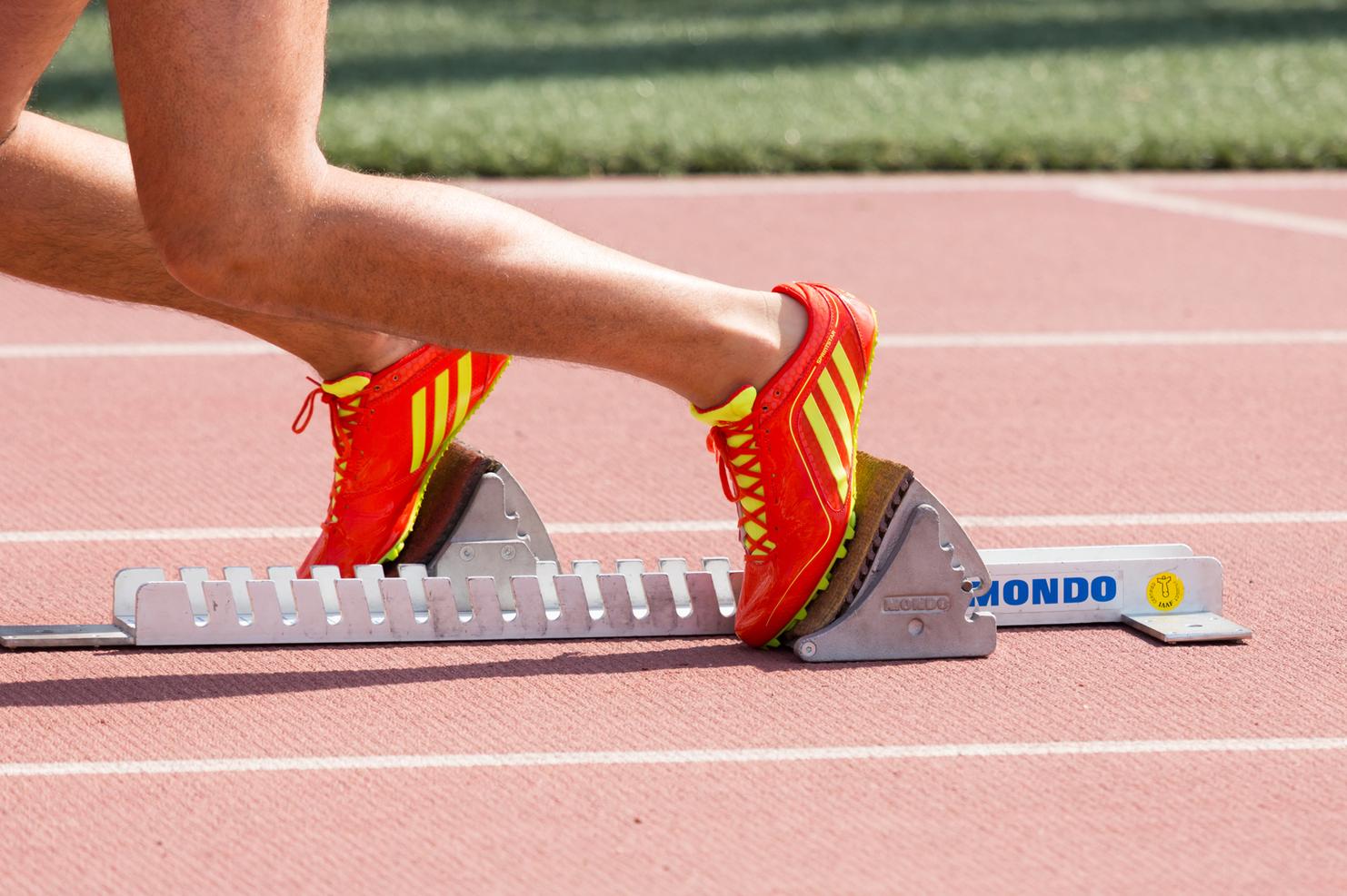 Nahaufnahme eines Fußes in einem roten Laufschuh, der auf einem Startblock auf einer Laufbahn steht.